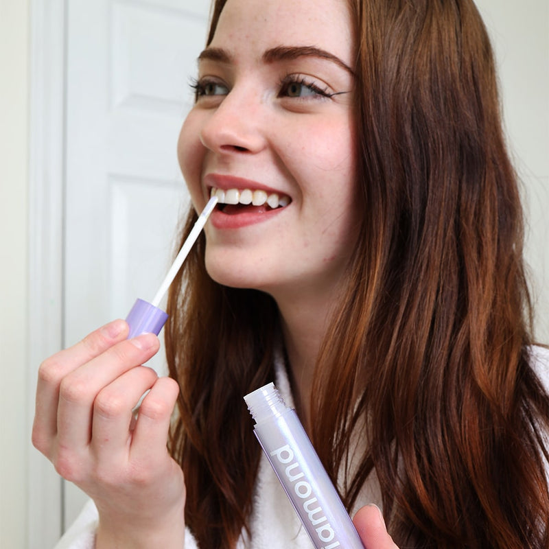 Nainen kylpyhuoneessa valkaiseva hehkutikku Diamond Smile stä kädessään