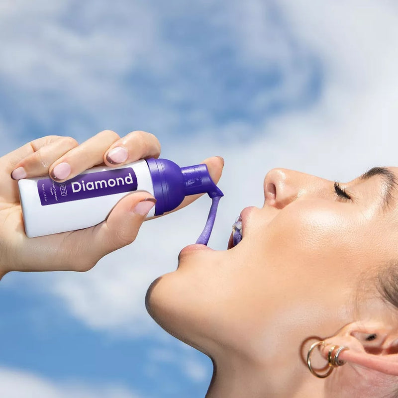 Nainen, jolla on Diamond Smile violetti hampaiden valkaiseva värinkorjausvaahto kädessään